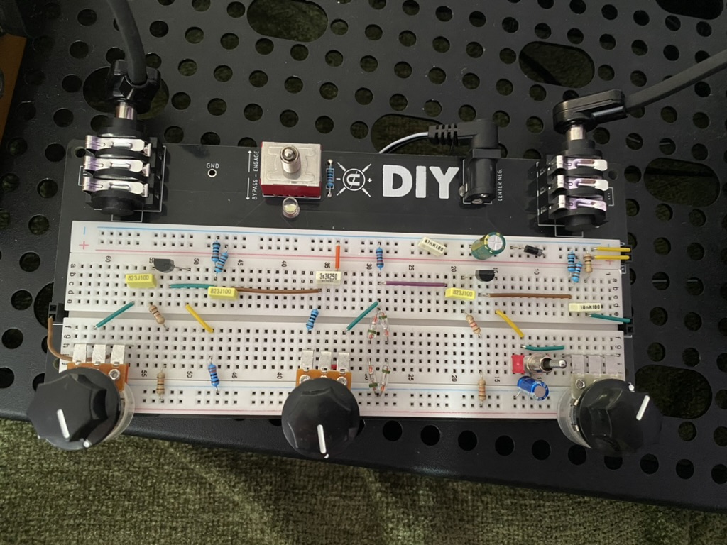 Picture of electronics breadboard with lots of components attached, namely resistors, capacitors, and other things. Several audio jacks are connected.